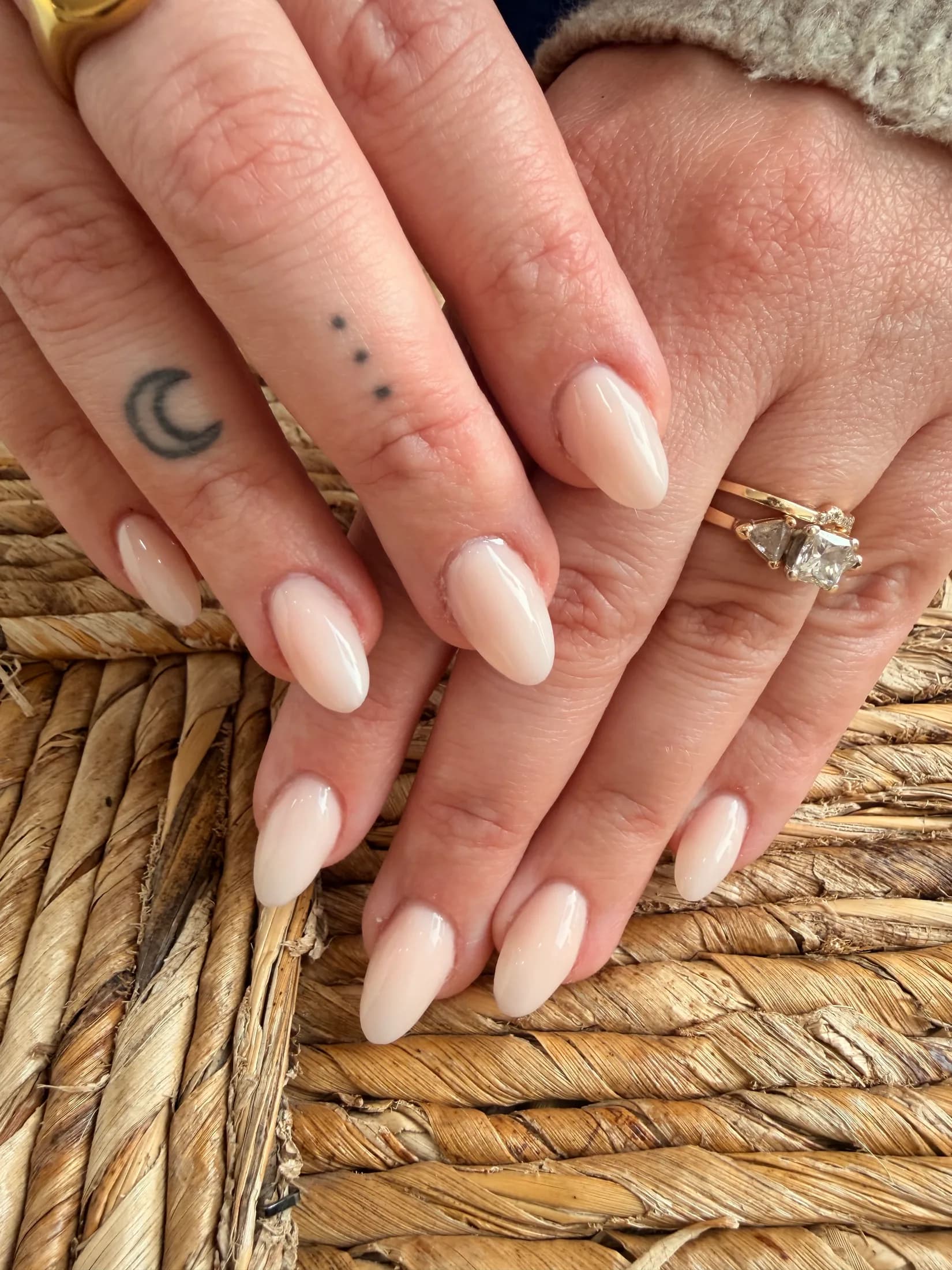 Nude almond manicure with a diamond ring on woven seagrass.